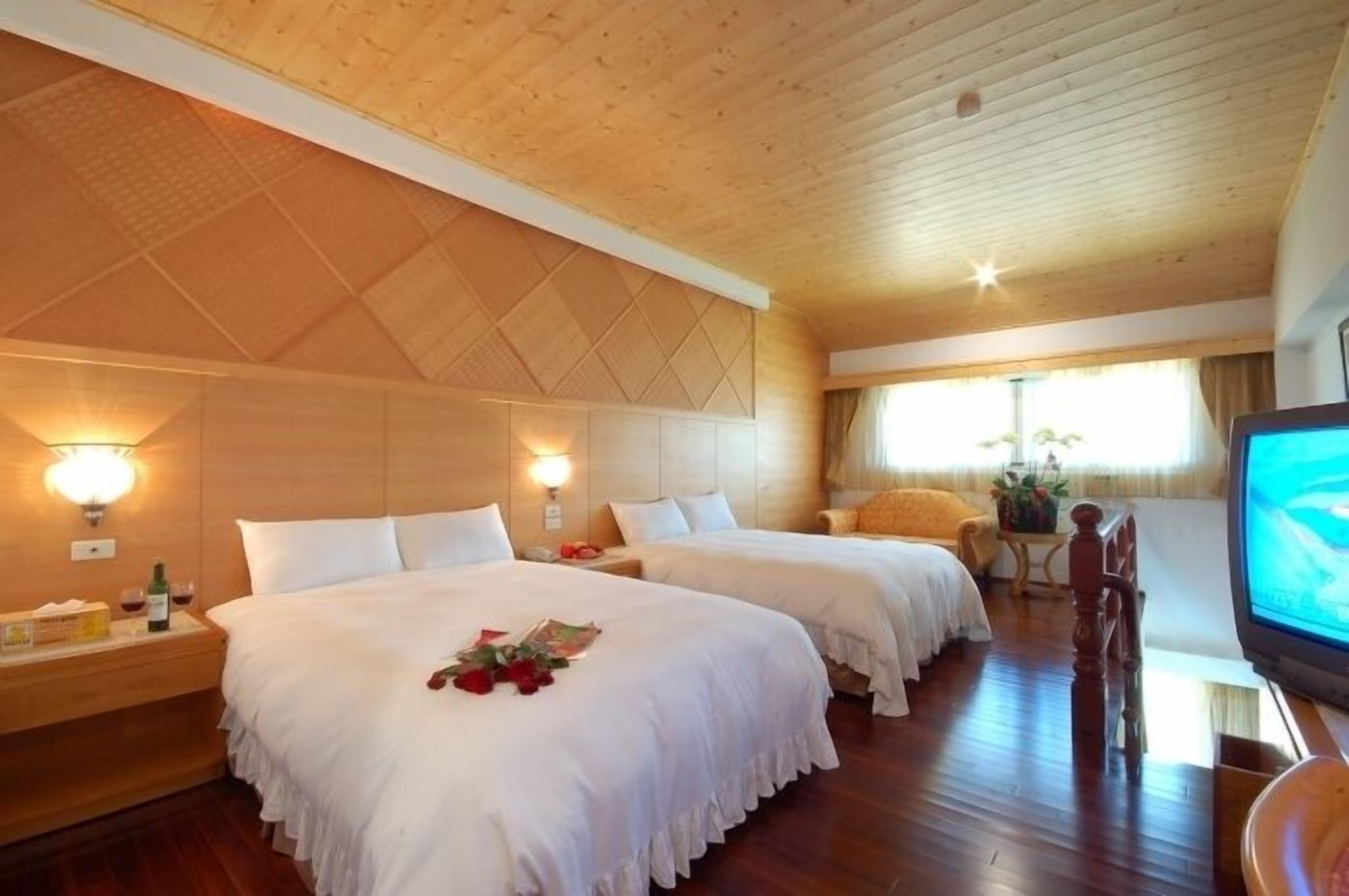 A hotel room with two beds, wooden ceiling, and a television.