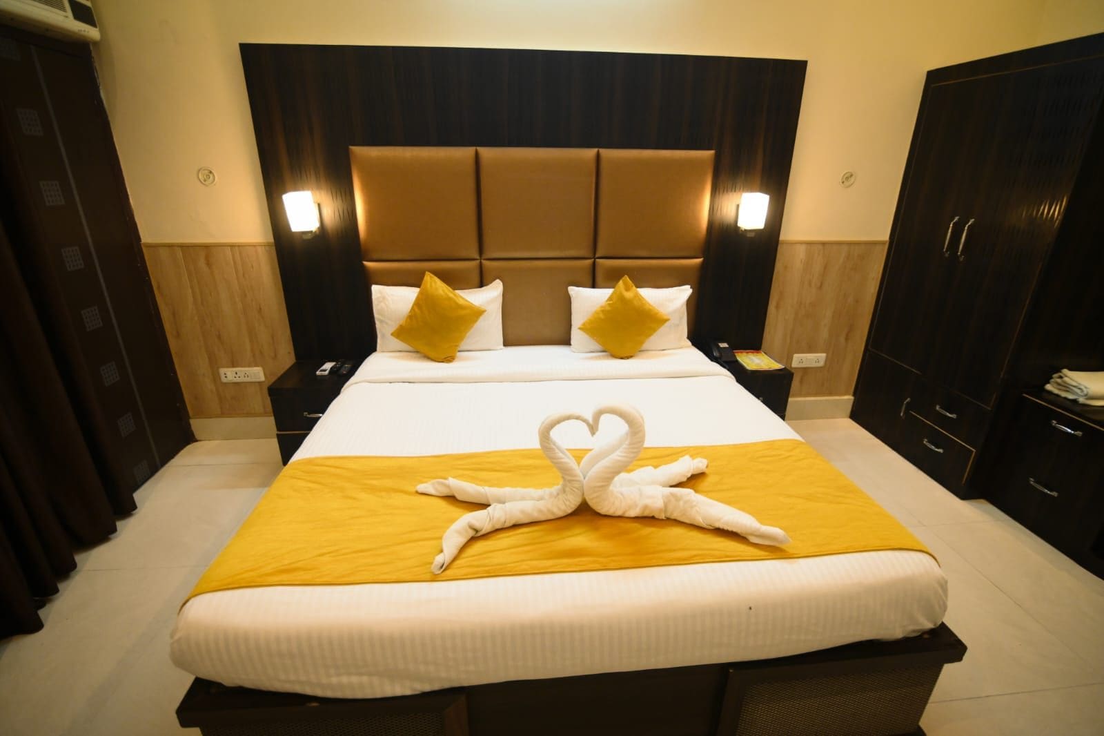 A hotel room with a large bed, a headboard, bedside tables, and a wardrobe.