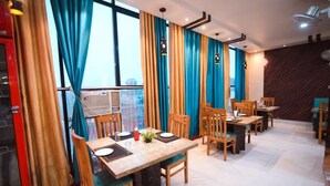 Un comedor con mesas y sillas de madera, ventanas amplias con cortinas azules y un diseño moderno en el techo.