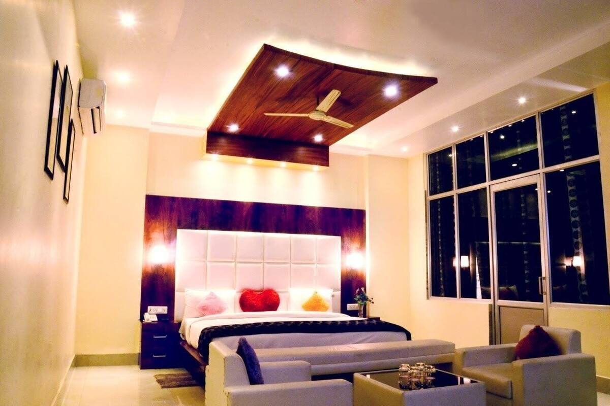Um quarto moderno com uma cama grande, um ventilador de teto, uma mesinha de cabeceira, um sofá e uma janela ampla.