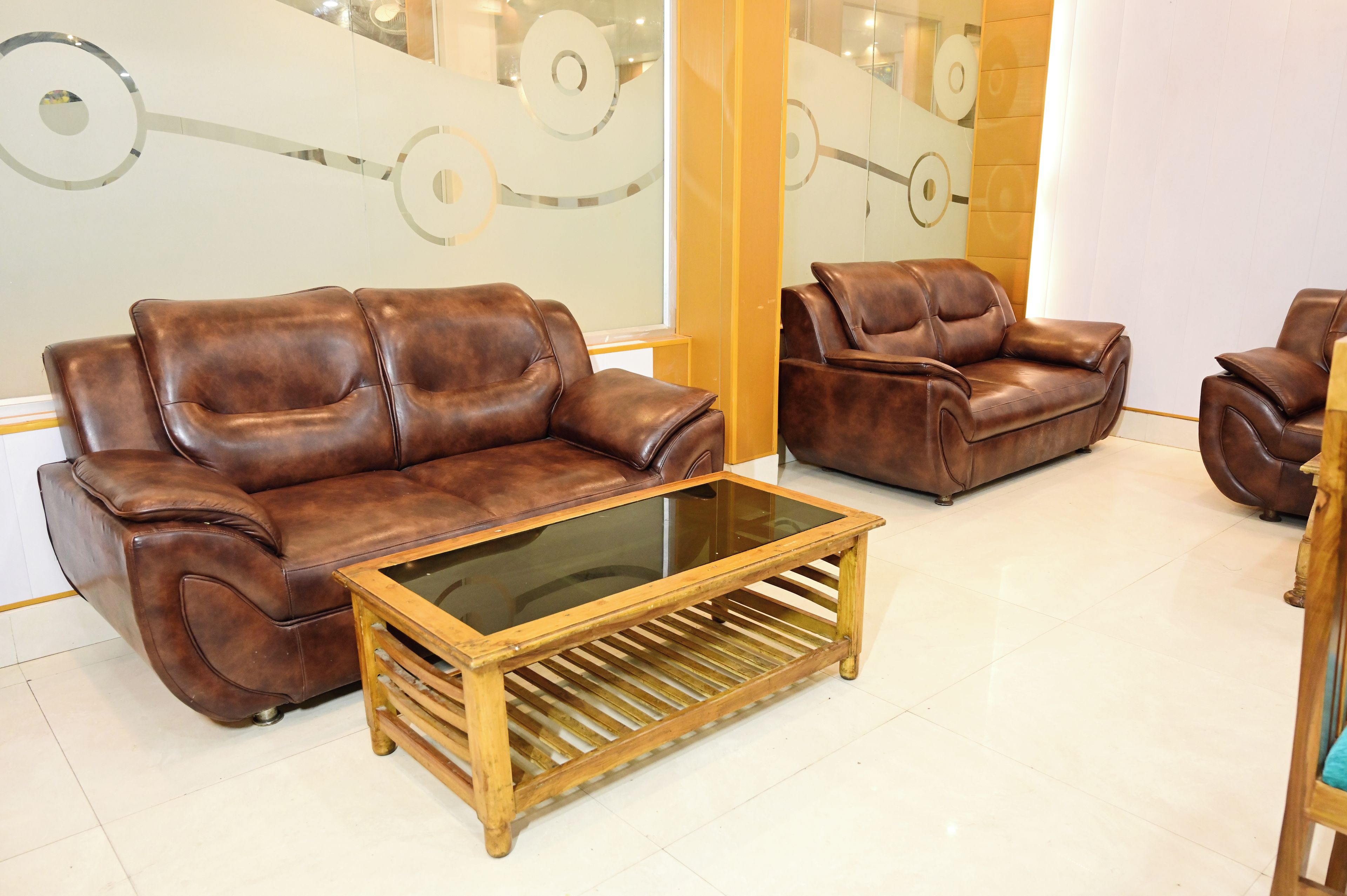 Un salon avec un canapé en cuir marron, une table basse en verre et une table d’appoint en bois.