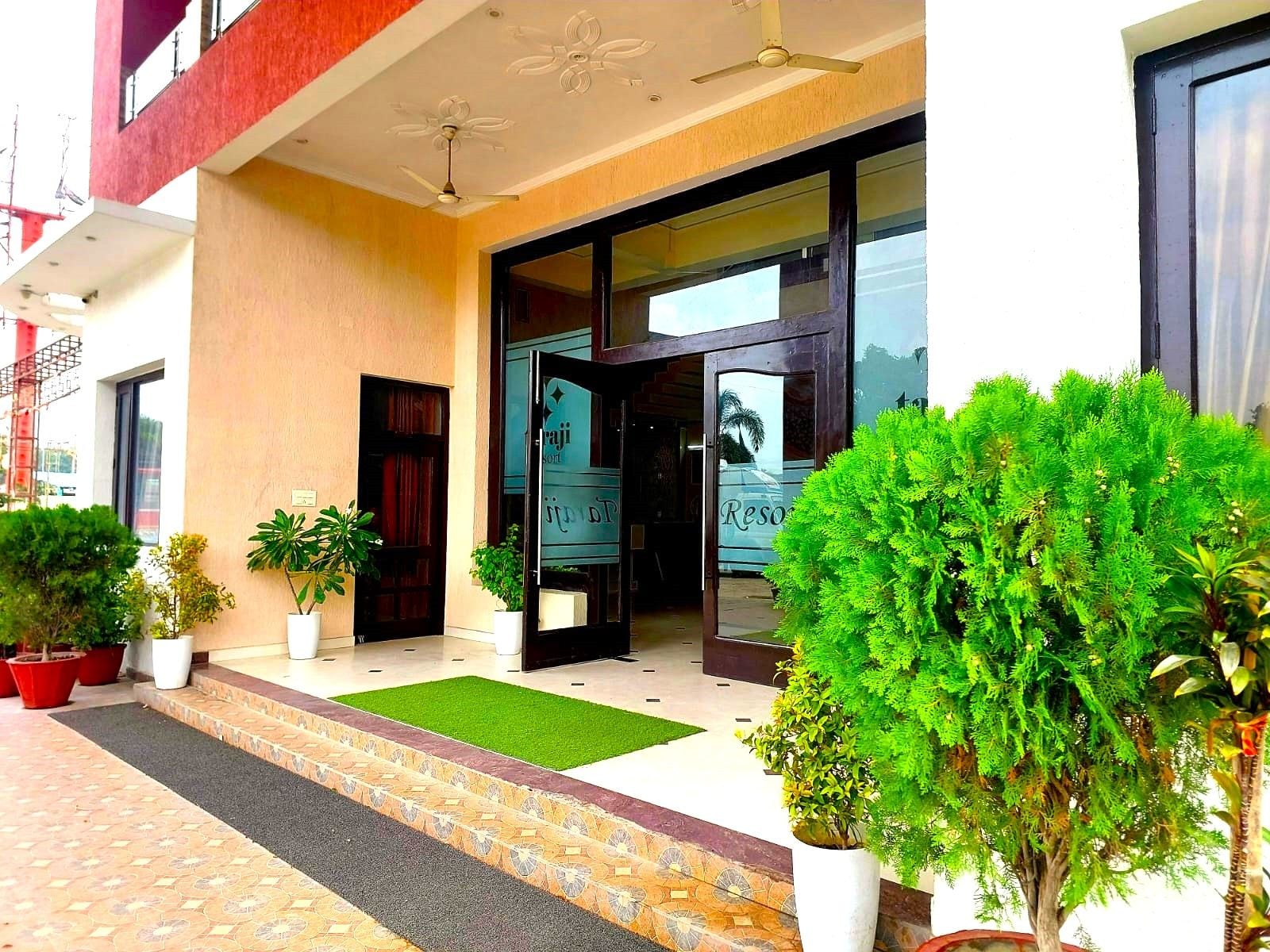 A hotel entrance with a modern design, featuring a glass door, a green carpet, and potted plants.