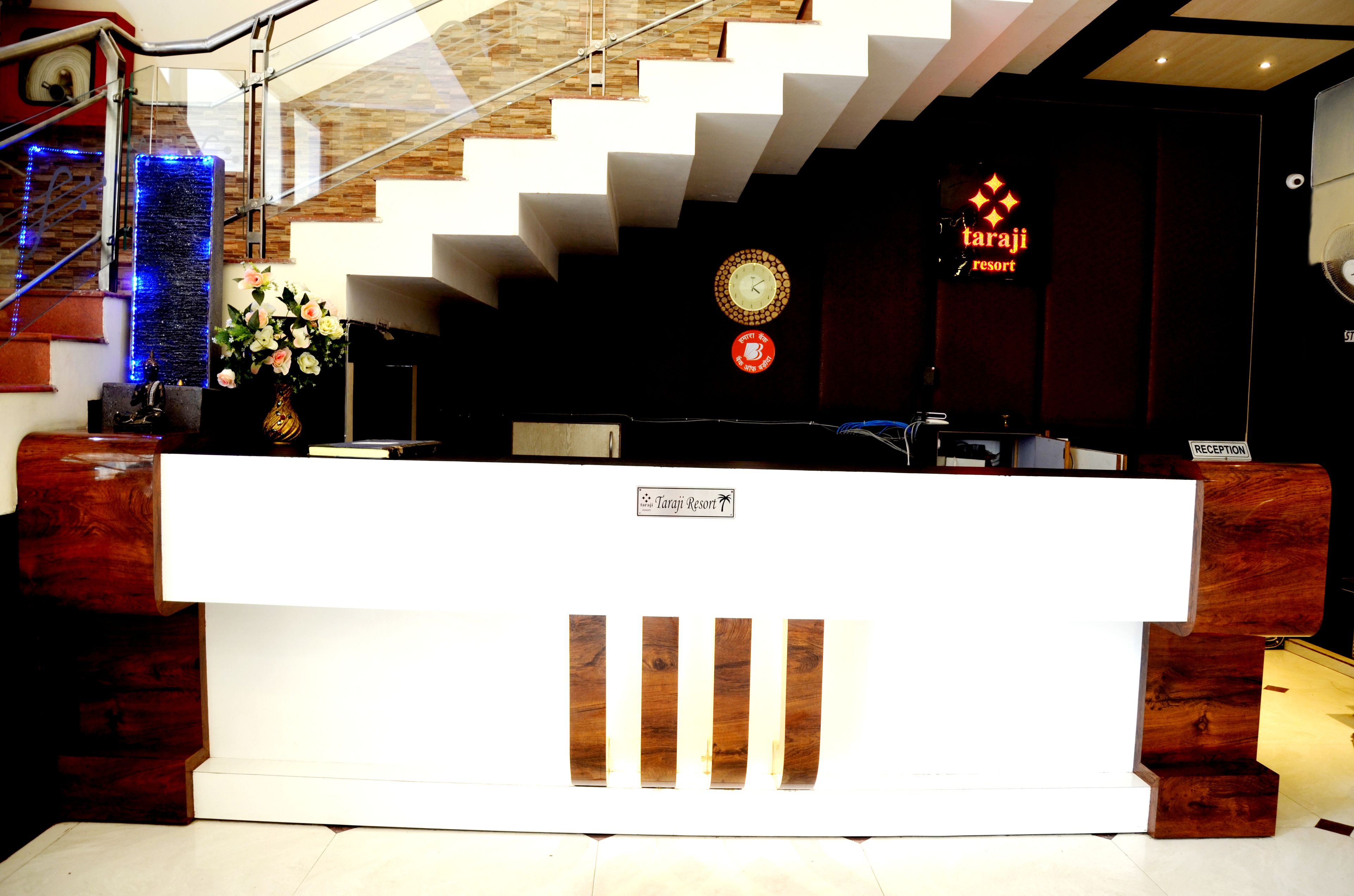 Un mostrador de recepción con un reloj, un cartel que indica Taraji Resort y una escalera con iluminación azul.