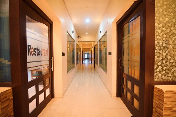 A hotel corridor with glass doors on either side, a tiled floor, and a patterned wall on the right.