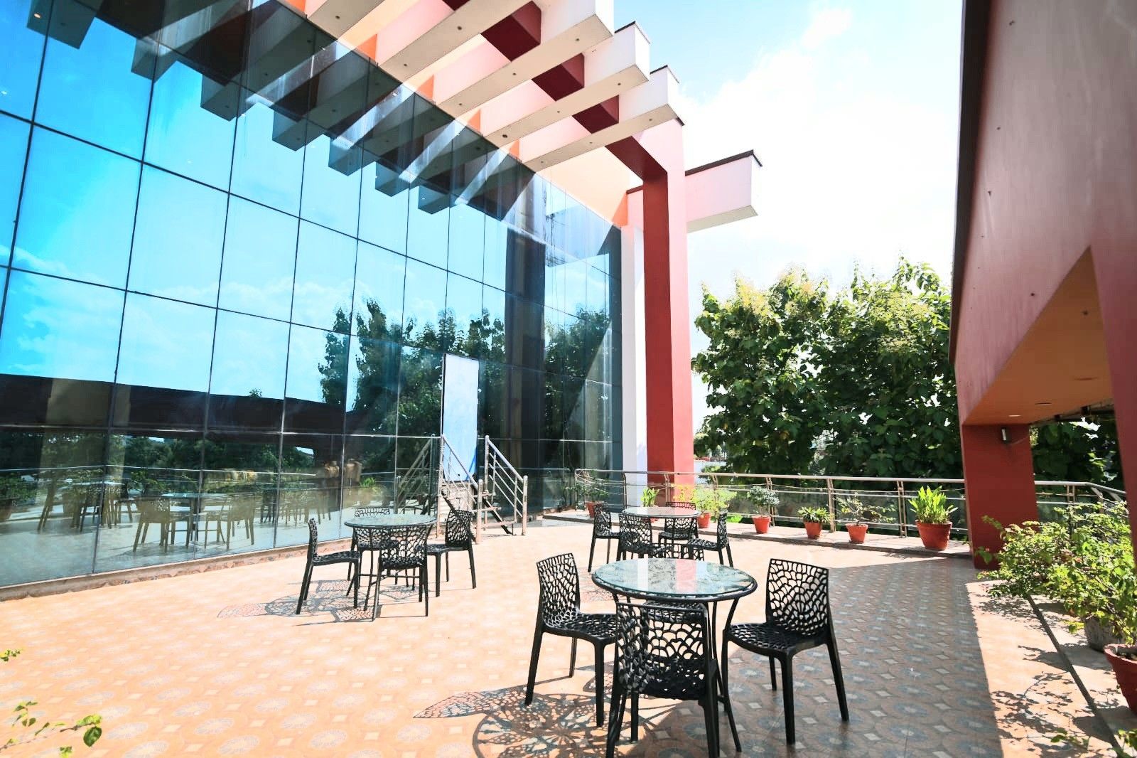 An outdoor seating area with tables and chairs, a glass building facade, and potted plants.