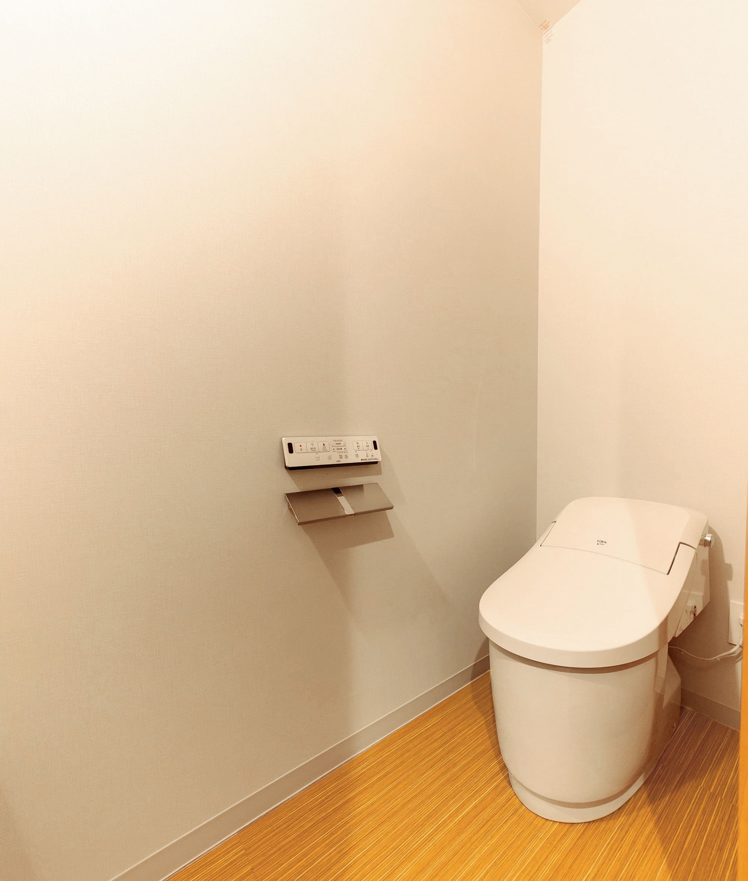A small, clean bathroom with a toilet, a wall-mounted electrical outlet, and a wooden floor.