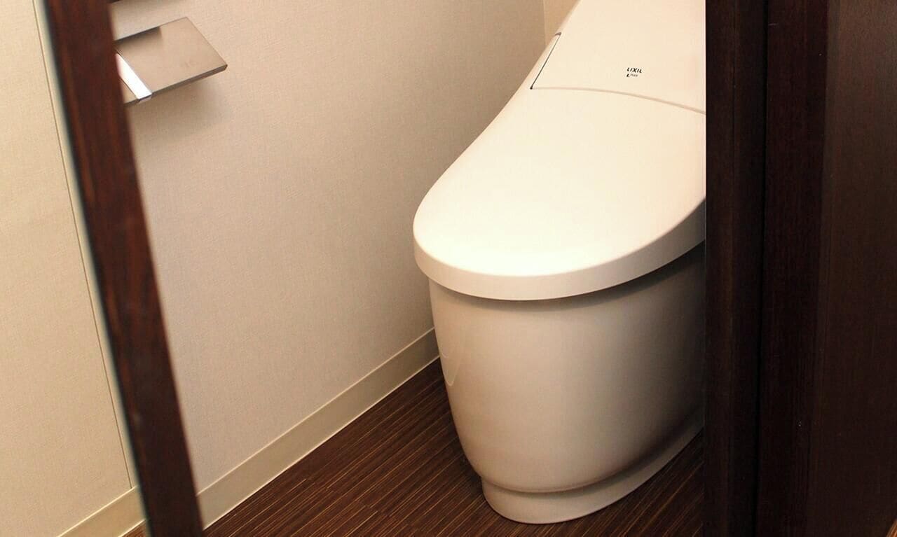 Eine weiße Toilette in einem Badezimmer mit Holzboden und einer beige farbenen Wand.