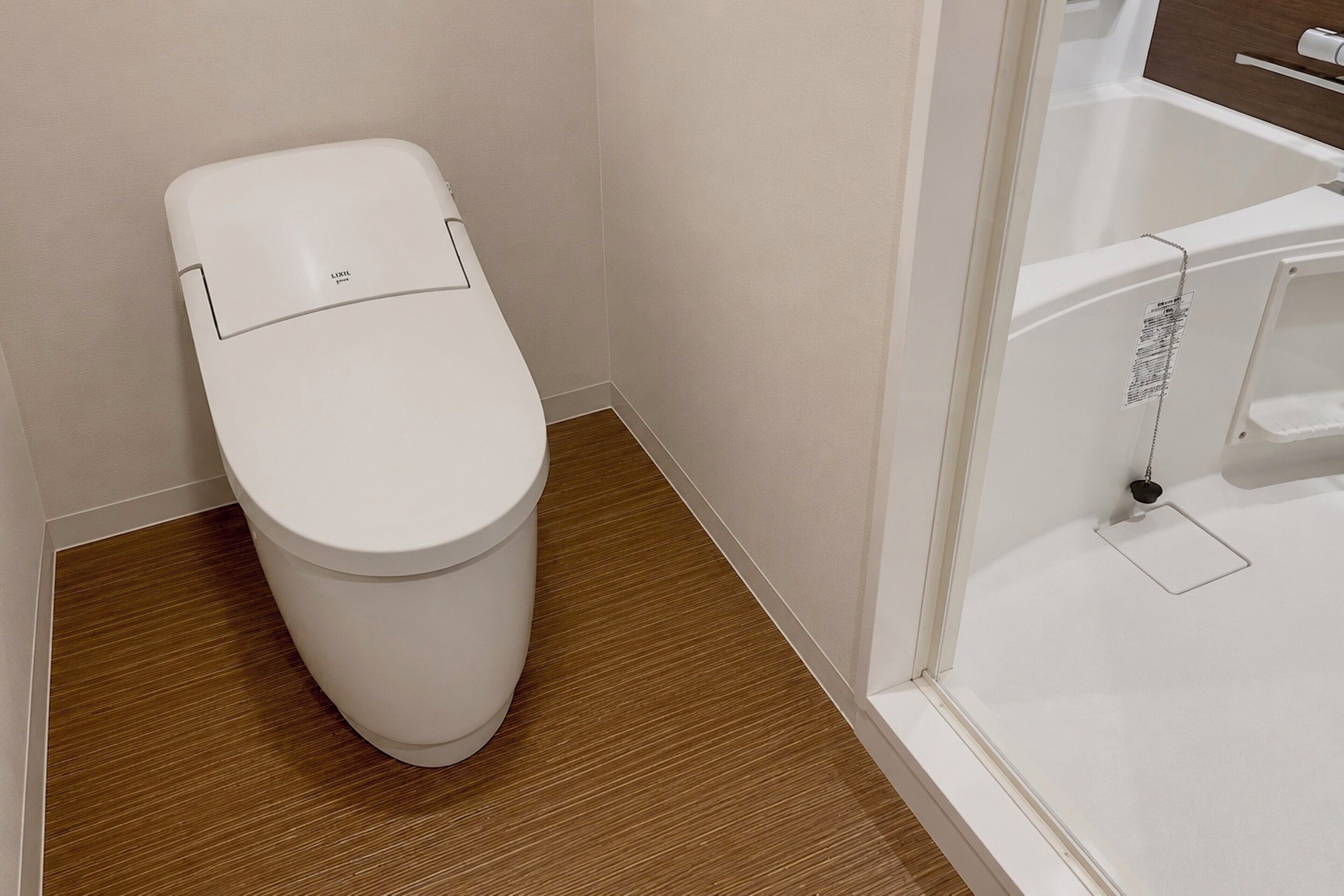 A white toilet, a wooden floor, and a white bathtub with a shower curtain.