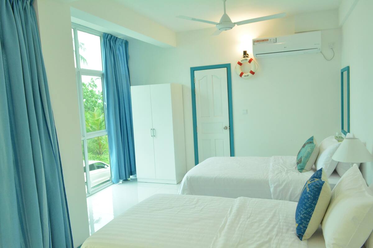 A hotel room with two beds, a ceiling fan, an air conditioning unit, and a view of the outside.