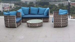 A balcony with a blue sofa set and two wicker chairs, a glass coffee table, and a city view. - Eclipse Residence Duplex (Cyberjaya)