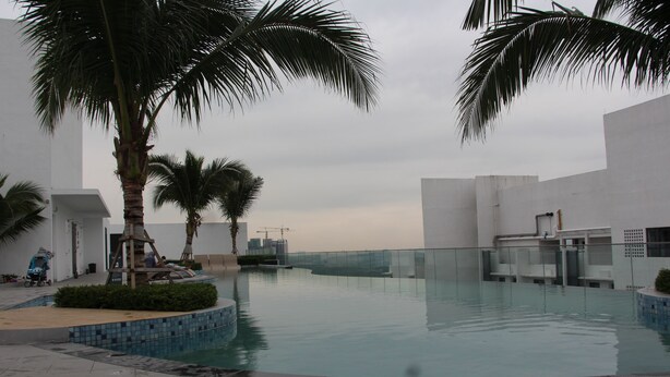 A swimming pool area with palm trees, tiled flooring, and a view of buildings in the background. - Eclipse Residence Duplex (Cyberjaya)