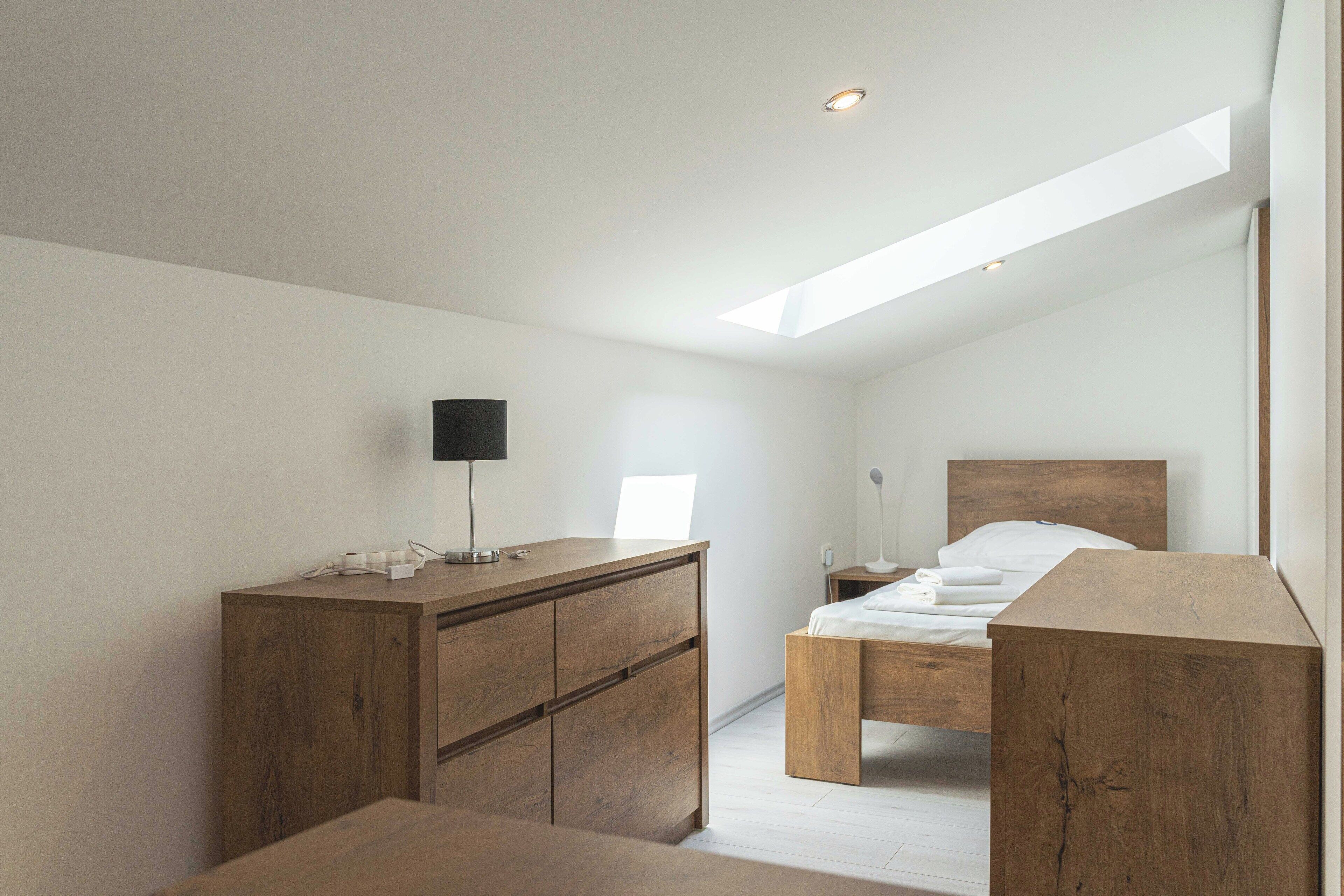 A bedroom with a skylight, wooden furniture, and a bedside table with a lamp.