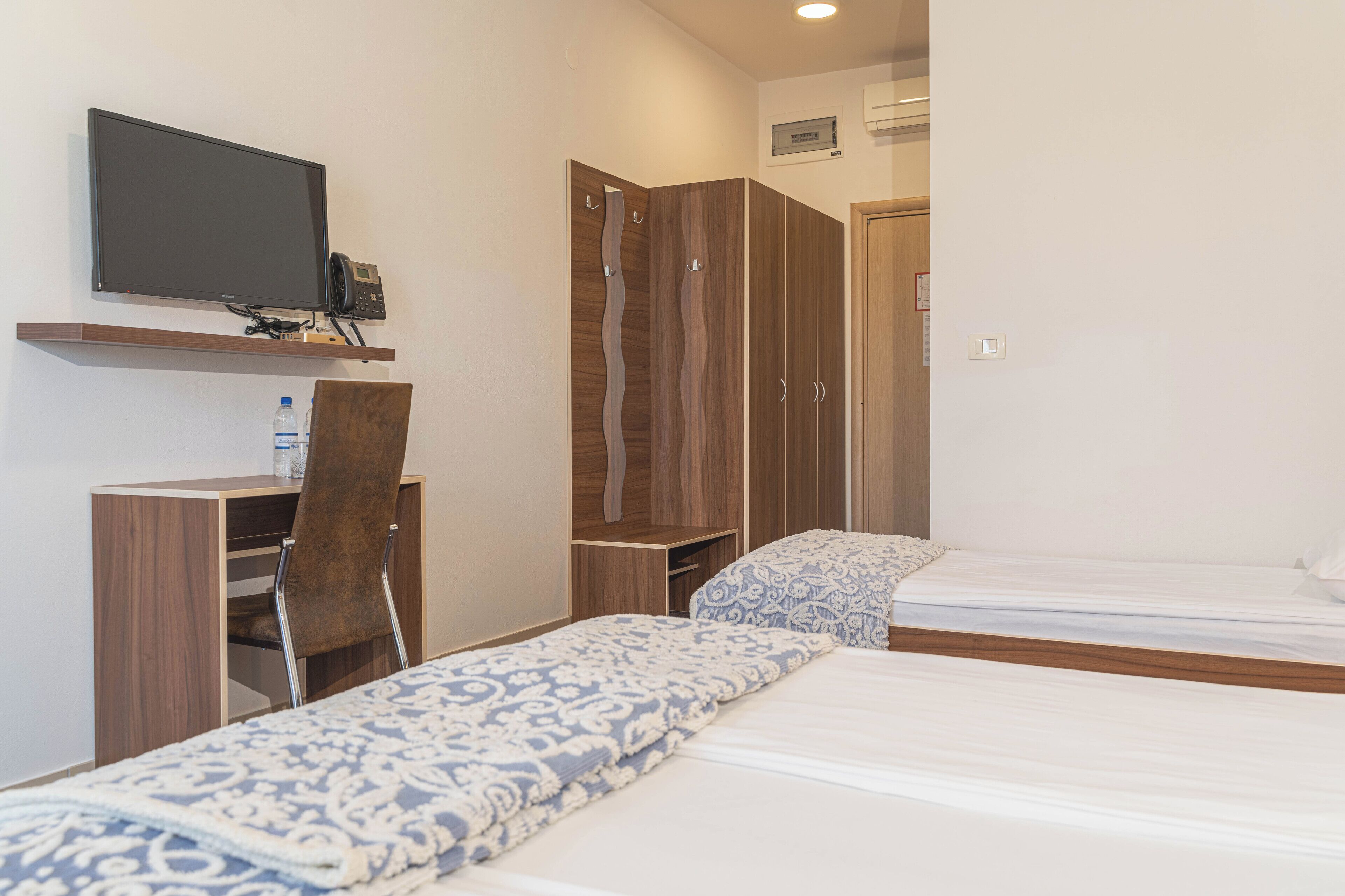 A hotel room with a bed, a desk with a chair, a television, and a wardrobe.