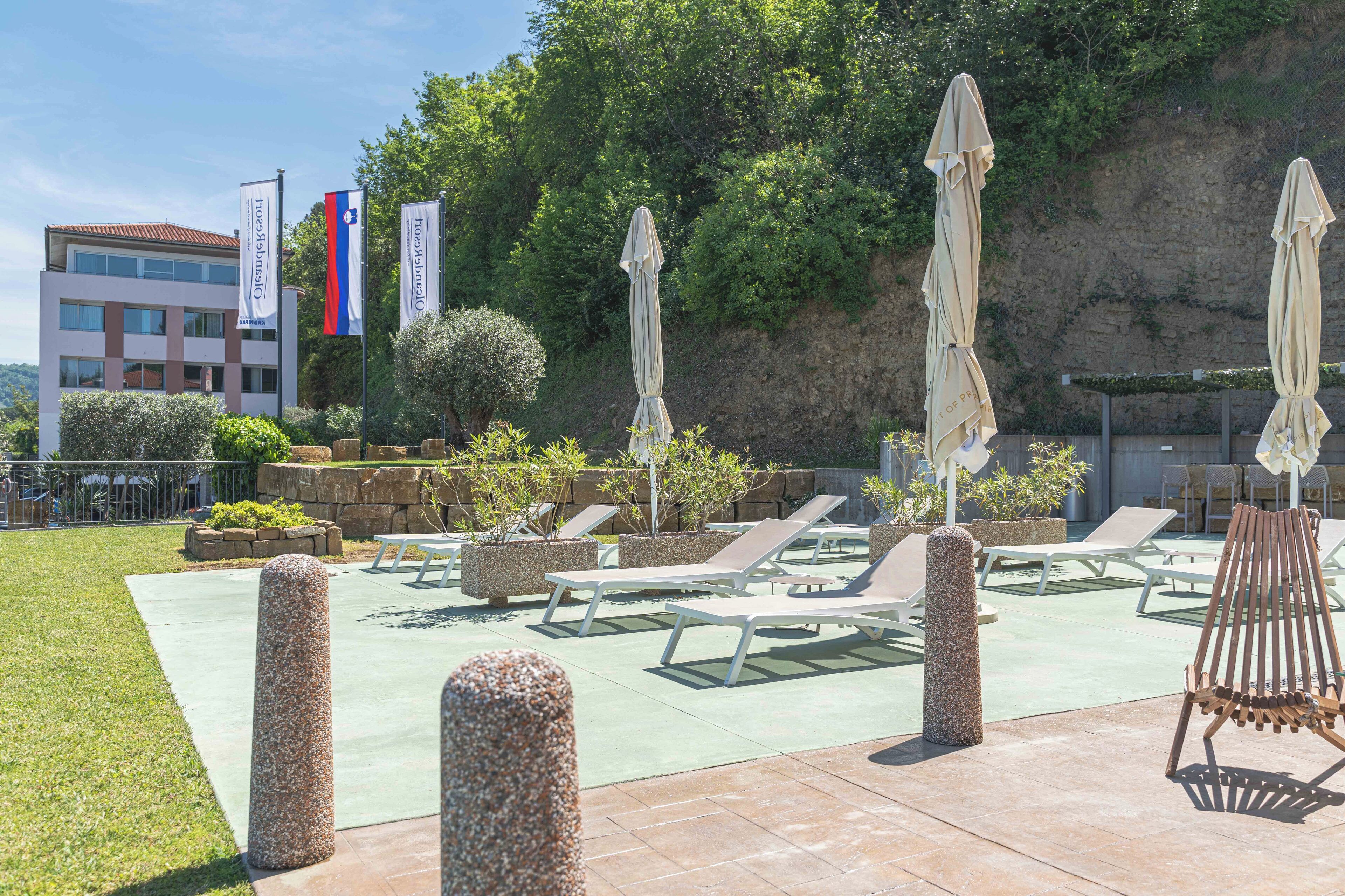 A rooftop lounge area with sun loungers, umbrellas, and a view of a building with flags.