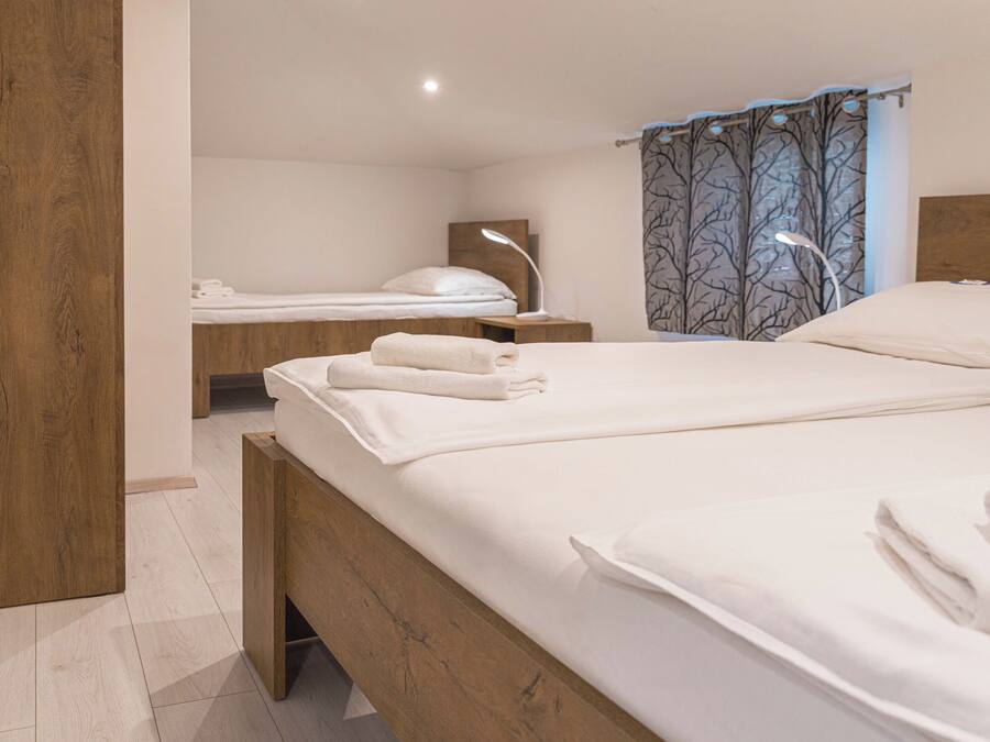 Ein Hotelzimmer mit einem großen Bett, einem kleineren Bett, einem Holzkopfstück, einem Nachttisch mit Lampe und einem Vorhang mit Baumdekor.