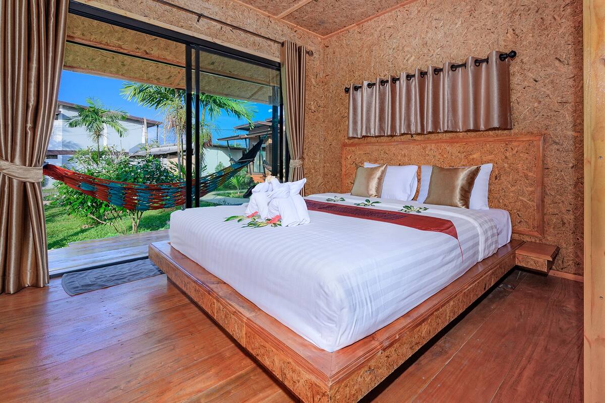 A bedroom with a large bed, a hammock, and a view of the outdoors.