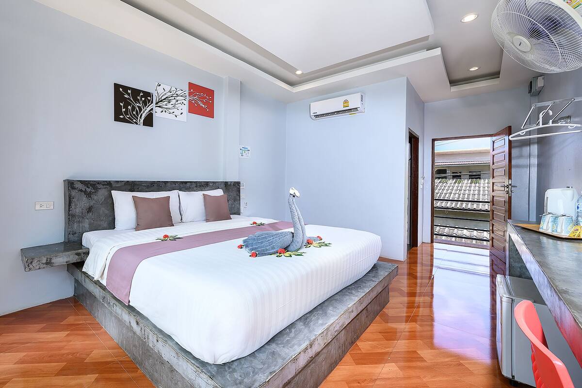 A modern hotel room with a large bed, a built-in bench, a ceiling fan, and a view of the outdoor area.