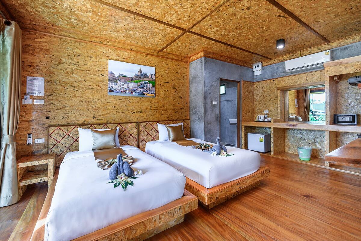 A room with two beds, wooden flooring, a picture on the wall, a small desk, and a bathroom area.