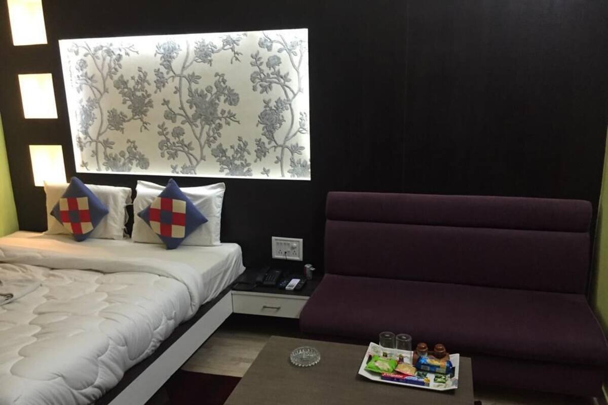 A hotel room with a bed, a sofa, a small table with snacks, and a window with floral wallpaper.