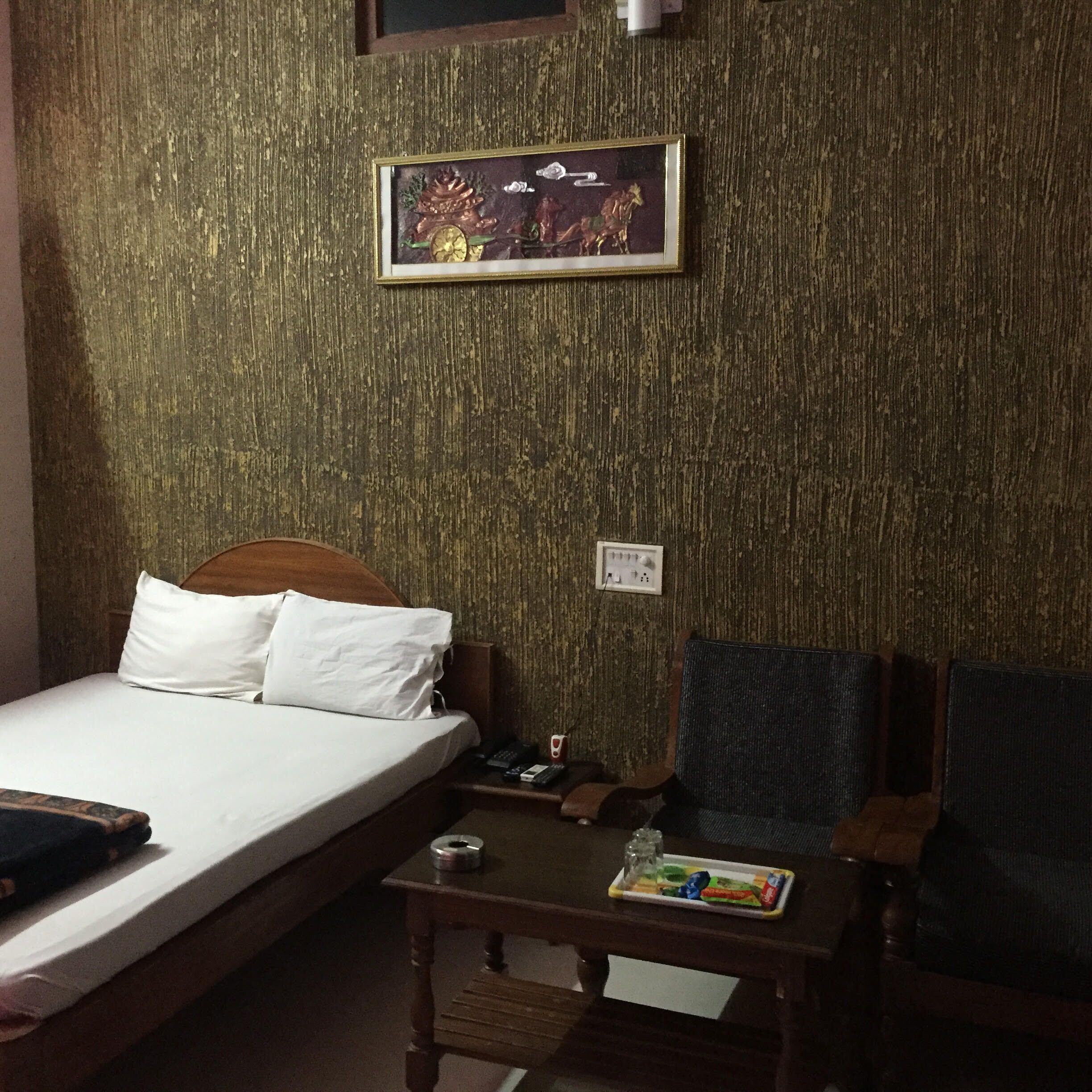 Een hotelkamer met een bed, een klein tafeltje met een afstandsbediening, een stoel en een aan de muur hangend schilderij.