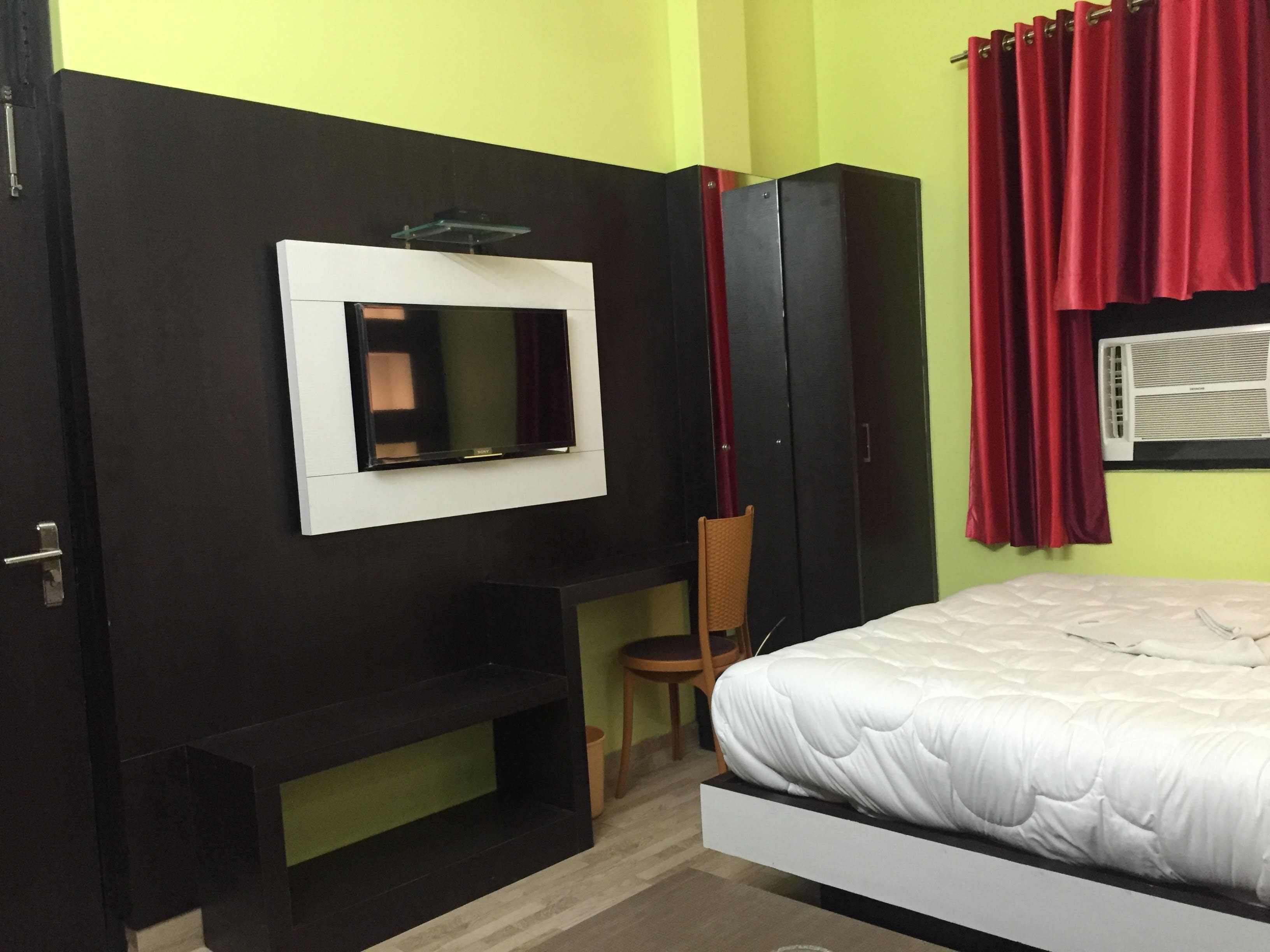 Ein Schlafzimmer mit Bett, Wandfernseher, Kleiderschrank und rotem Vorhang.