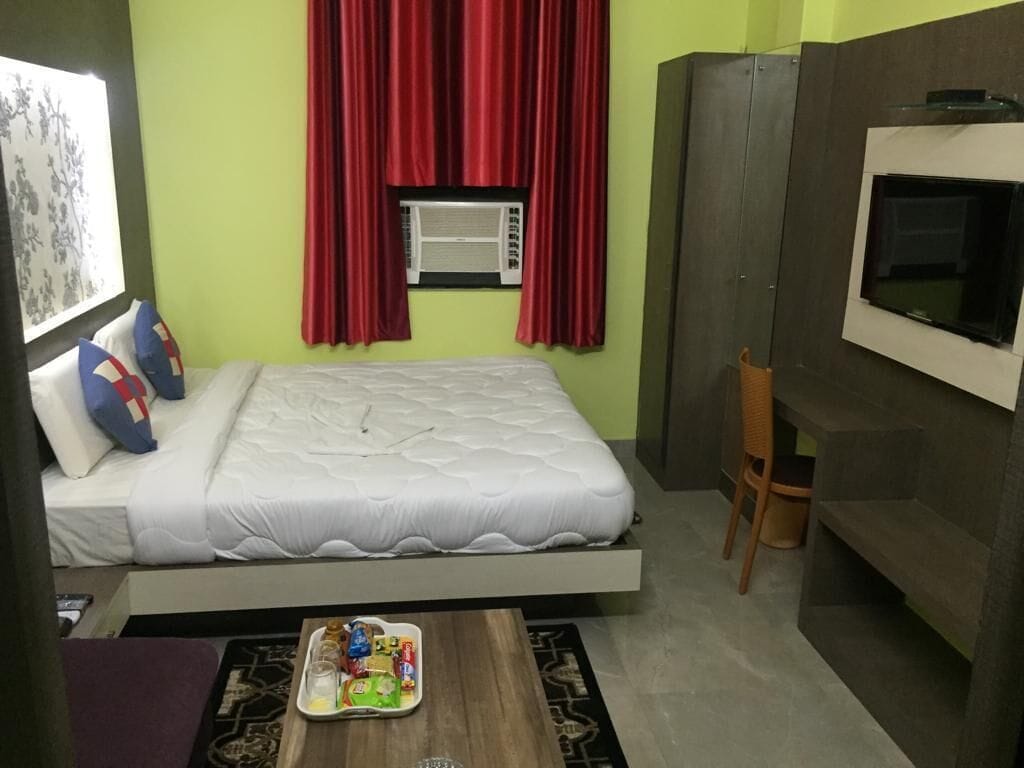 A bedroom with a bed, a TV mounted on the wall, and a window with red curtains.