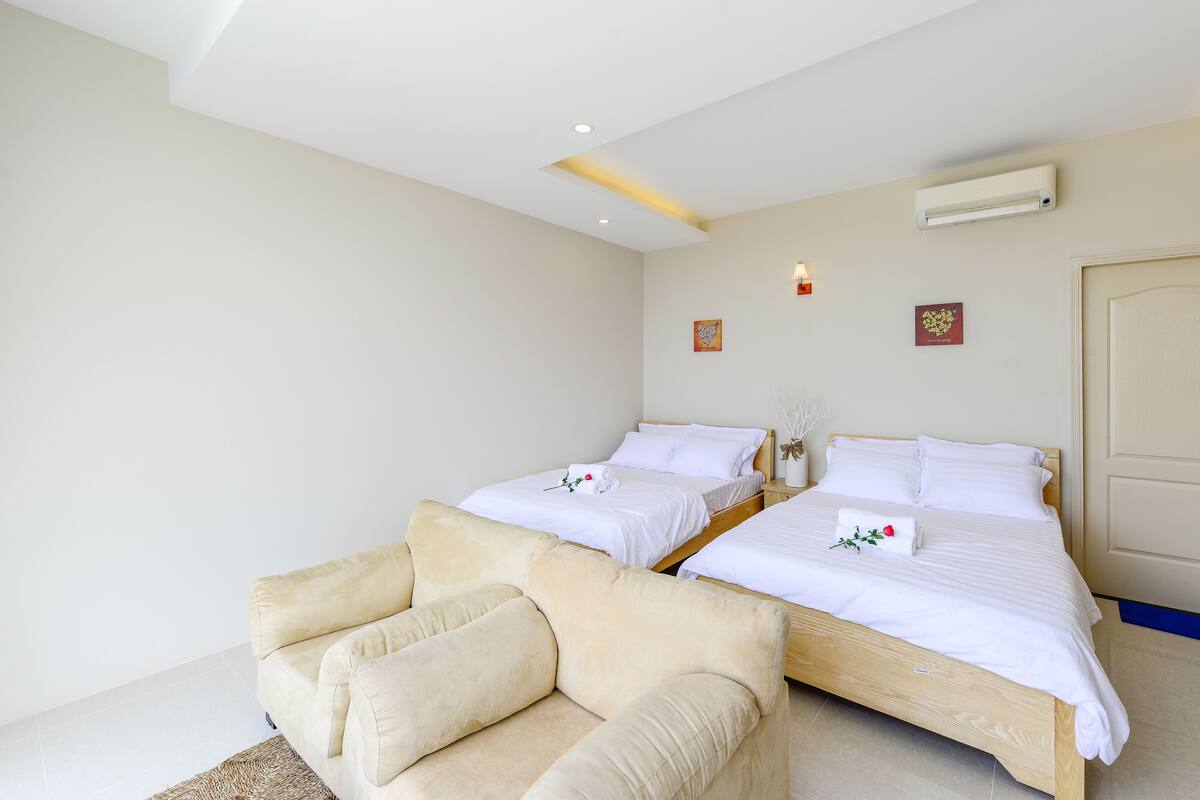 Une chambre d’hôtel avec deux lits, un canapé, un climatiseur fixé au mur et une porte.