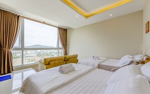 Ett hotellrum med två sängar, en soffa och utsikt över stadsbilden genom stora fönster.