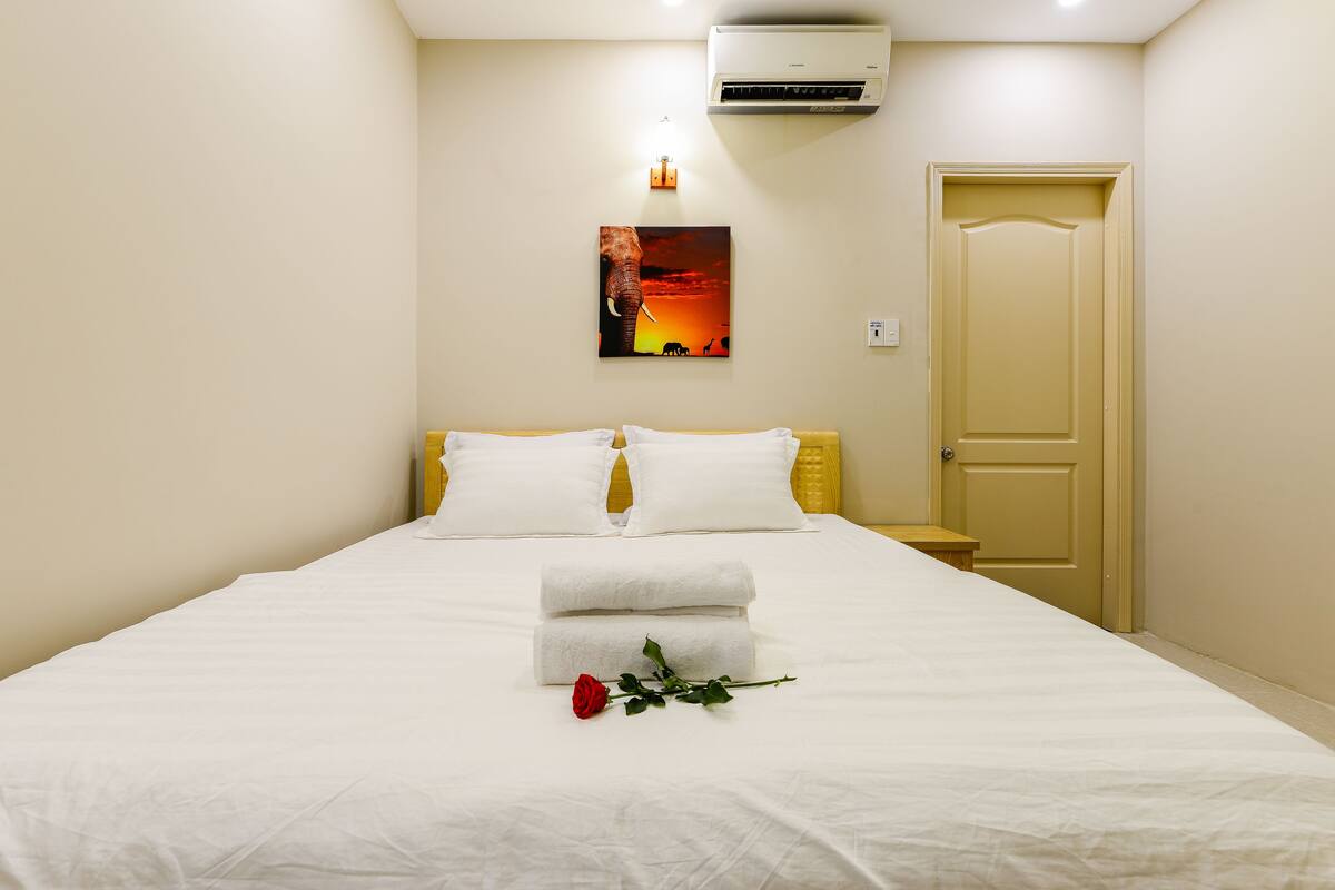 Un lit bien fait, avec des draps blancs, une seule rose rouge et deux serviettes pliées.