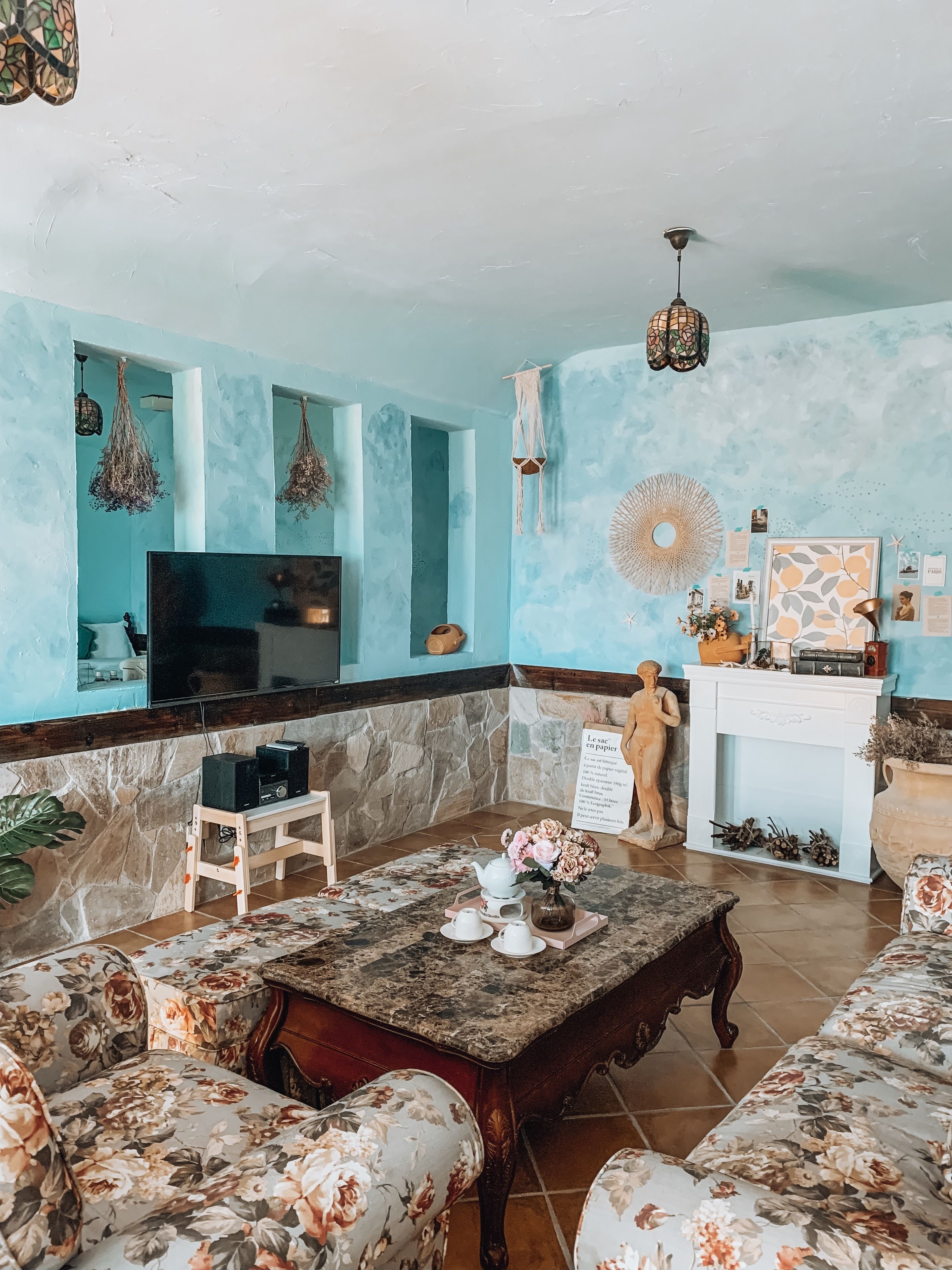 Una sala de estar con televisor, sofás con estampado floral, una mesita de centro y una chimenea.