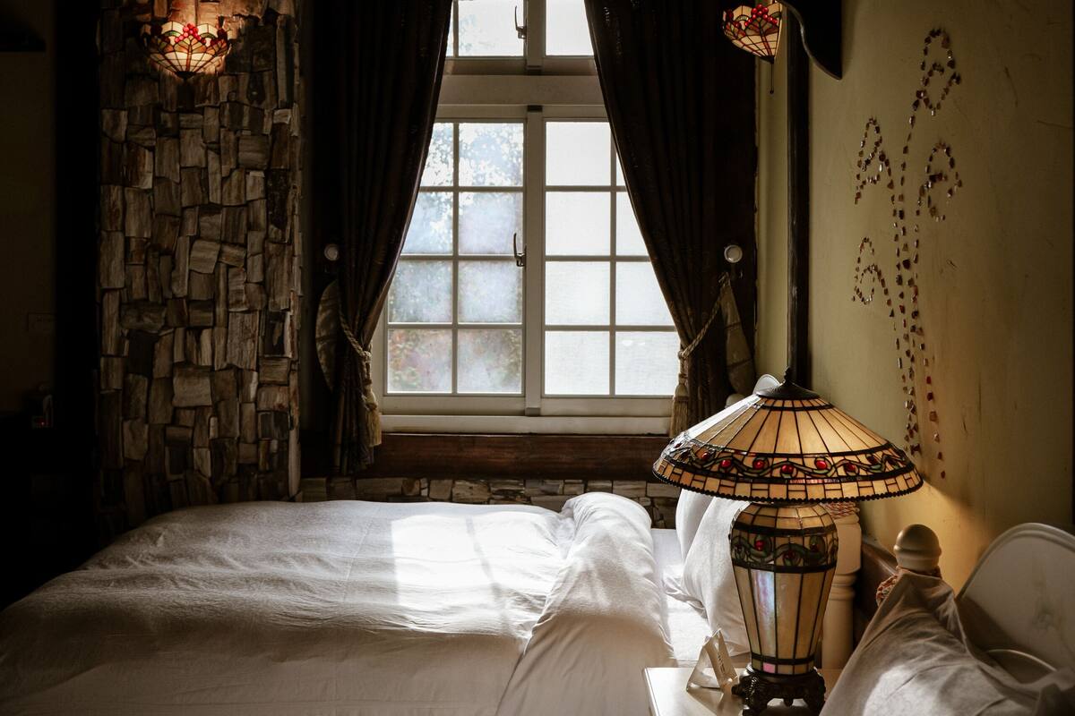 Een kamer met twee bedden, een stenen muur, een raam met gordijnen en een hanglamp.