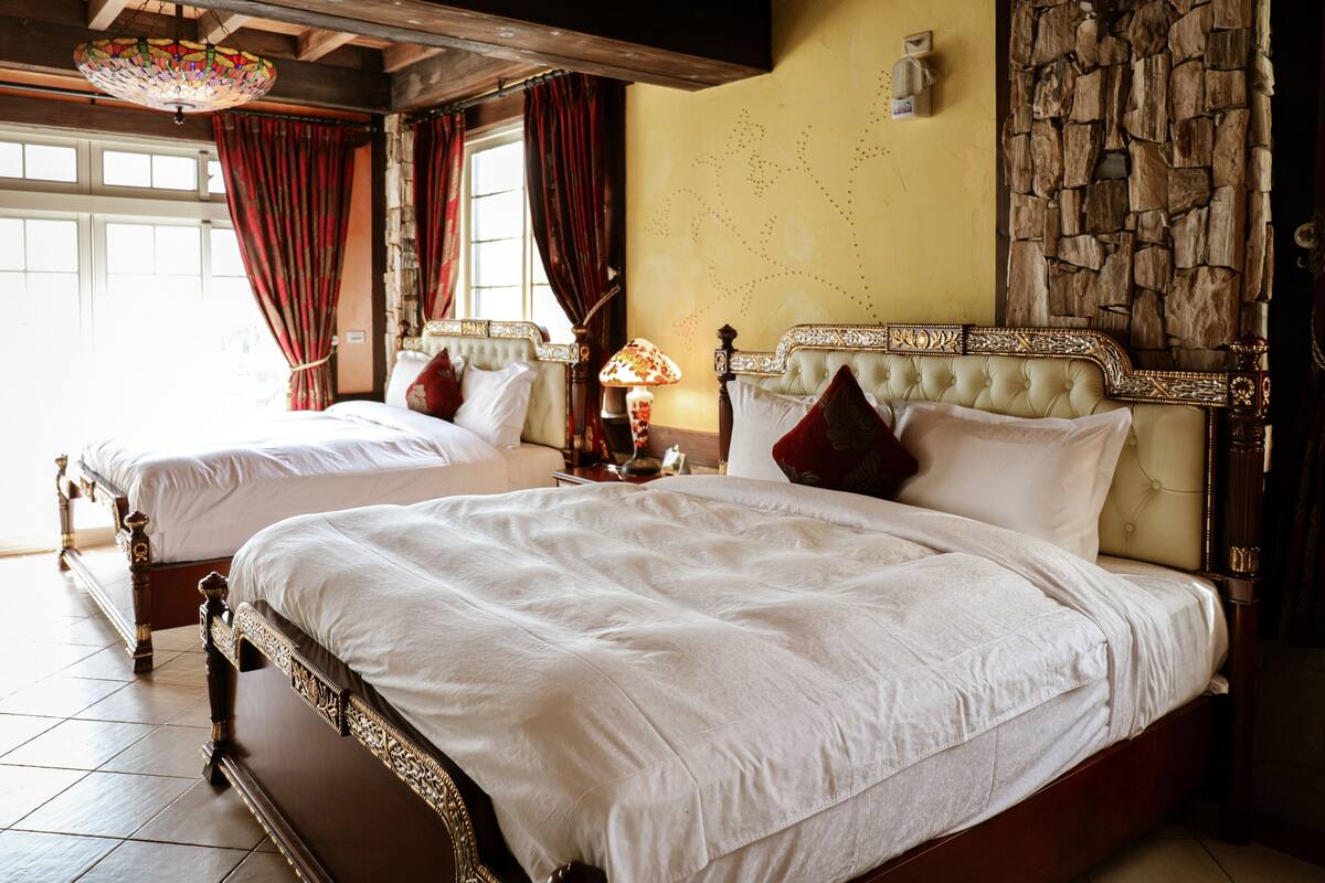 Een kamer met twee grote bedden, houten hoofdborden en een stenen muur.