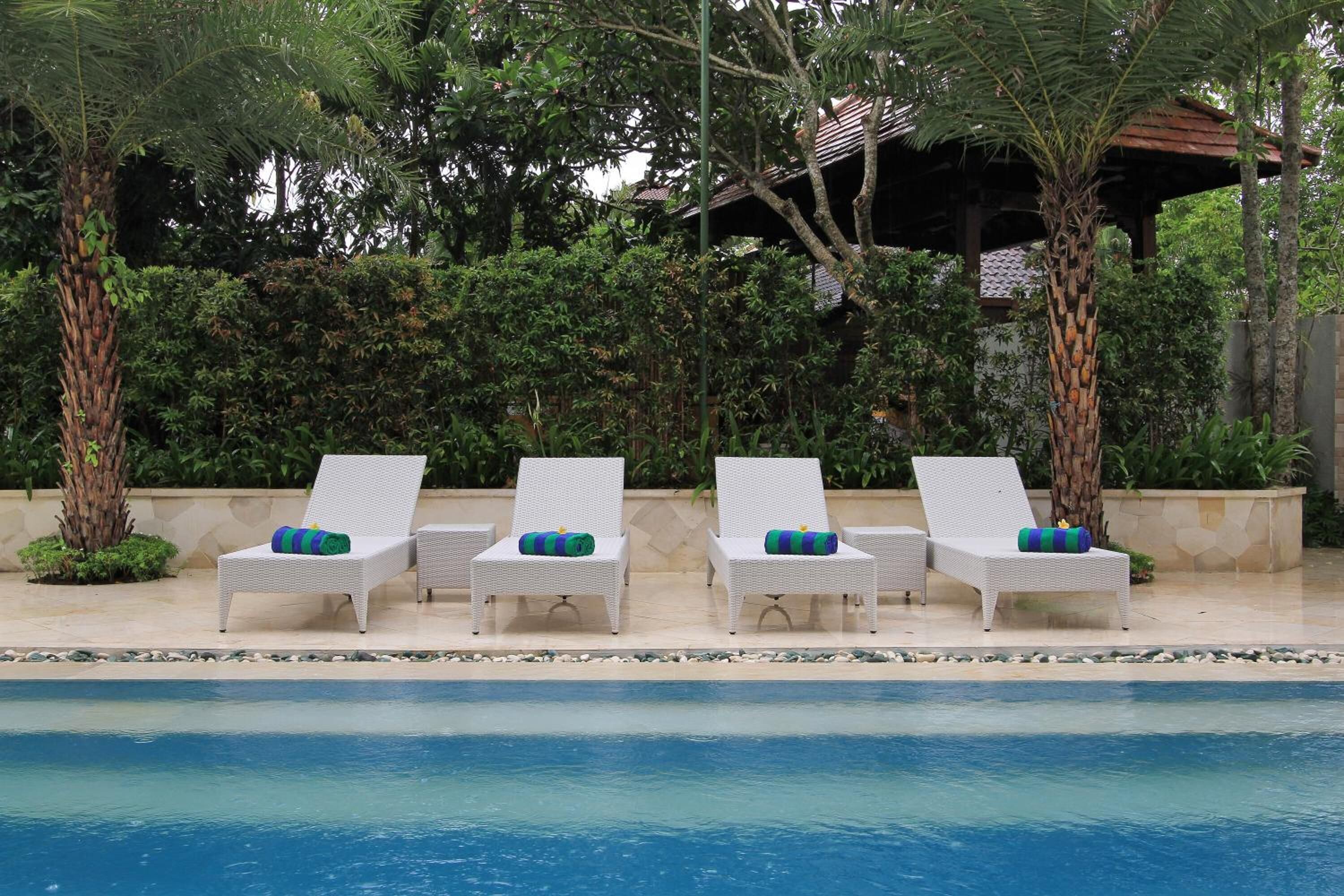 A poolside area with four white lounge chairs, each with a green and blue striped pillow.