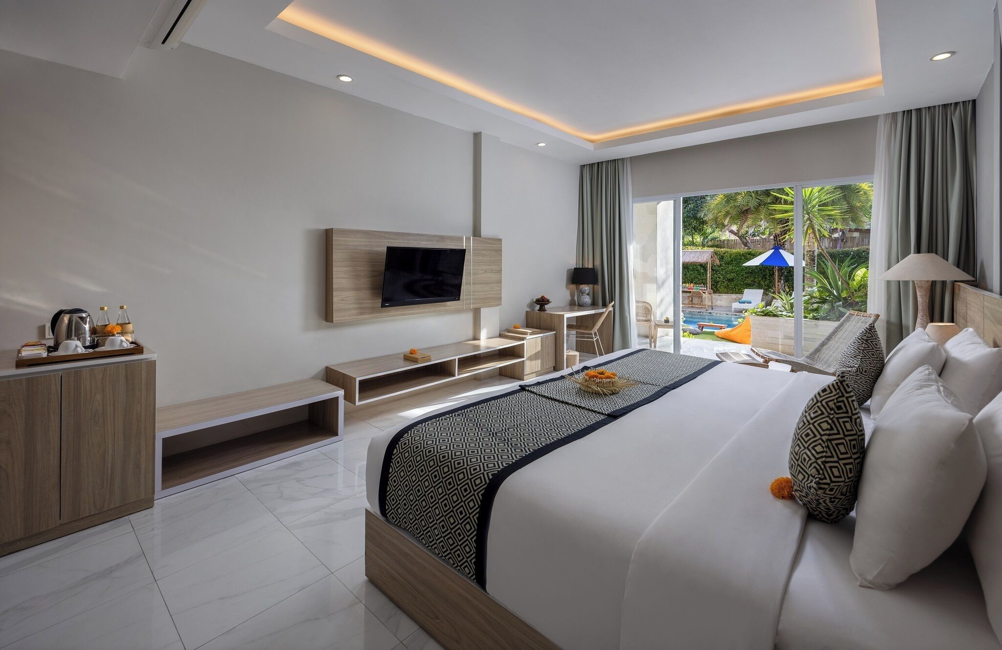 Une chambre d’hôtel moderne dotée d’un grand lit, d’un téléviseur fixé au mur, d’un bureau et offrant une vue sur l’espace extérieur de la piscine.