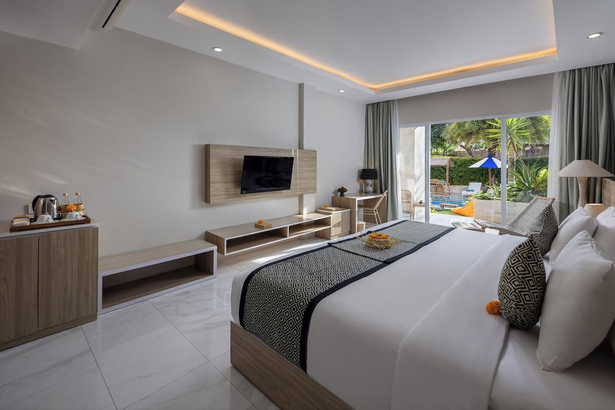 A modern hotel room with a large bed, a TV mounted on the wall, a desk, and a view of the outdoor pool area.