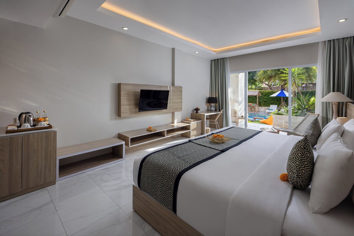 A modern hotel room with a large bed, a TV mounted on the wall, a desk, and a view of the outdoor pool area.