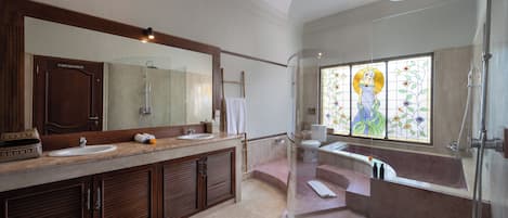 A modern bathroom with a large mirror, two sinks, a bathtub, and a stained glass window.