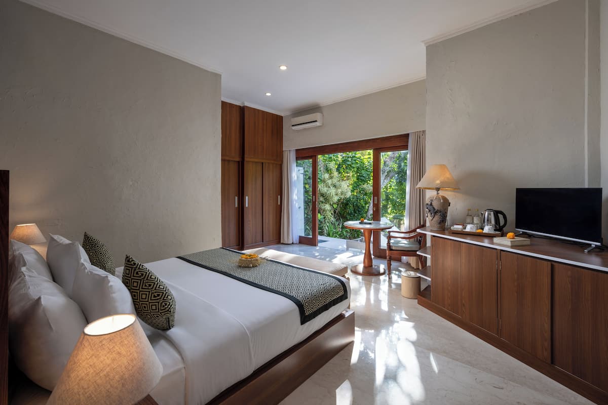 A modern bedroom with a large bed, bedside lamps, a TV, and a view of greenery outside.