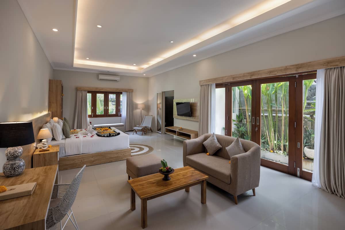 A modern living room with a sofa, coffee table, and a bed with a view of greenery outside.