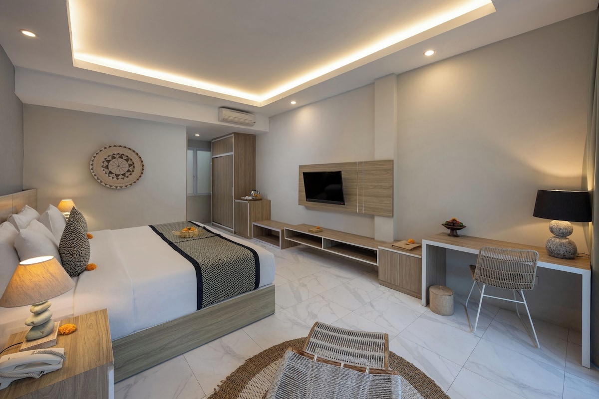 Una habitación de hotel moderna con cama, mesita de noche, lámpara, televisor y un rincón de descanso con una silla y una mesa.