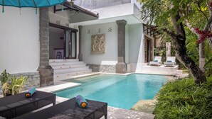 Un espace piscine avec des chaises longues, un escalier menant à un balcon et une végétation luxuriante.