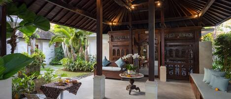 A covered outdoor area with a wooden ceiling, seating arrangements, and potted plants.