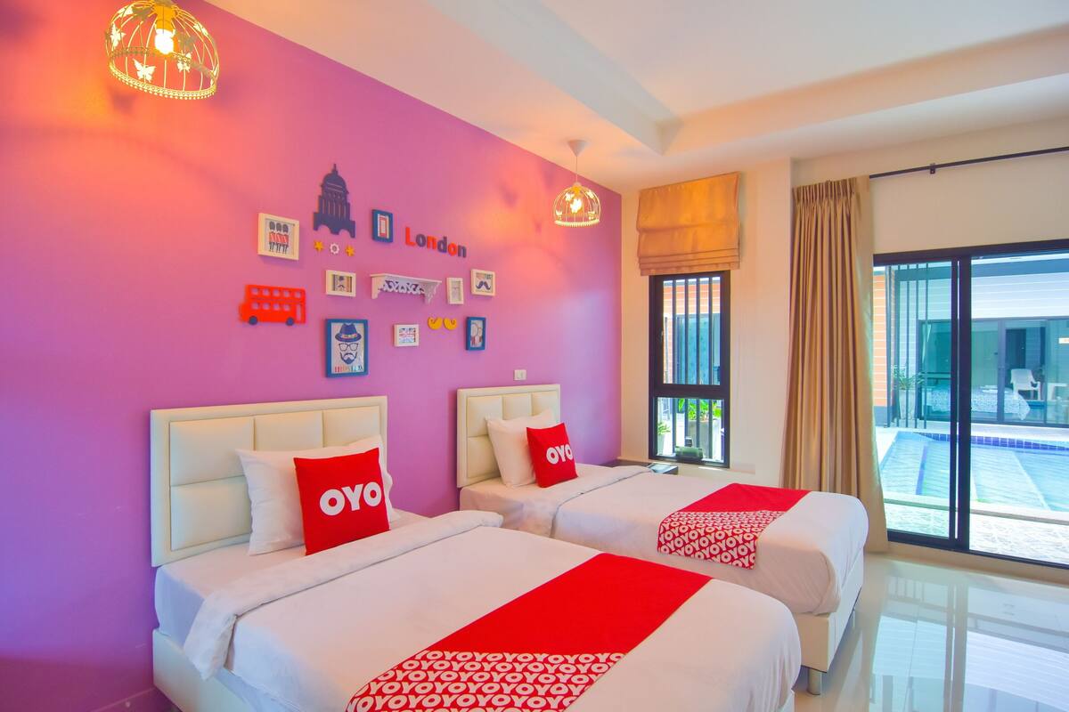 A hotel room with two beds, a purple wall, and a view of a pool.