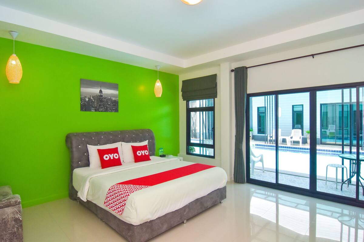 A modern hotel room with a large bed, bright green walls, and a view of the outdoor area.