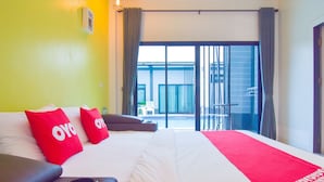 A hotel room with a bed, red pillows, a red blanket, and a view of a balcony and outdoor area. - OYO 500 Cordelia Resort Samroiyod (Sam Roi Yot)