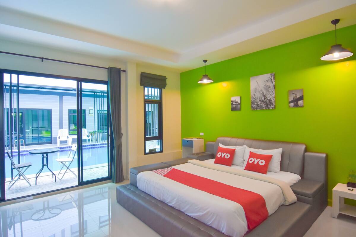 A modern hotel room with a large bed, a view of the pool, and bright green walls.