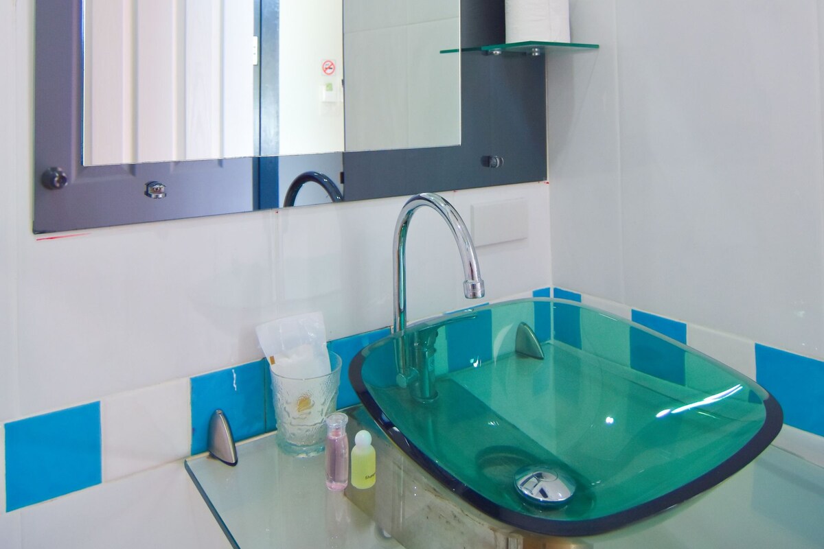 A bathroom with a glass sink, a mirror, and a toilet paper holder.