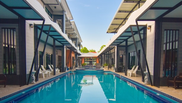 A modern hotel pool area with a clear view of the pool, two wooden benches facing the pool, and a covered seating area with chairs. - OYO 500 Cordelia Resort Samroiyod (Sam Roi Yot)