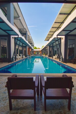 Zona de piscina moderna de hotel, con vista despejada a la piscina, dos bancos de madera orientados hacia ella, y un área de estar cubierta con sillas.