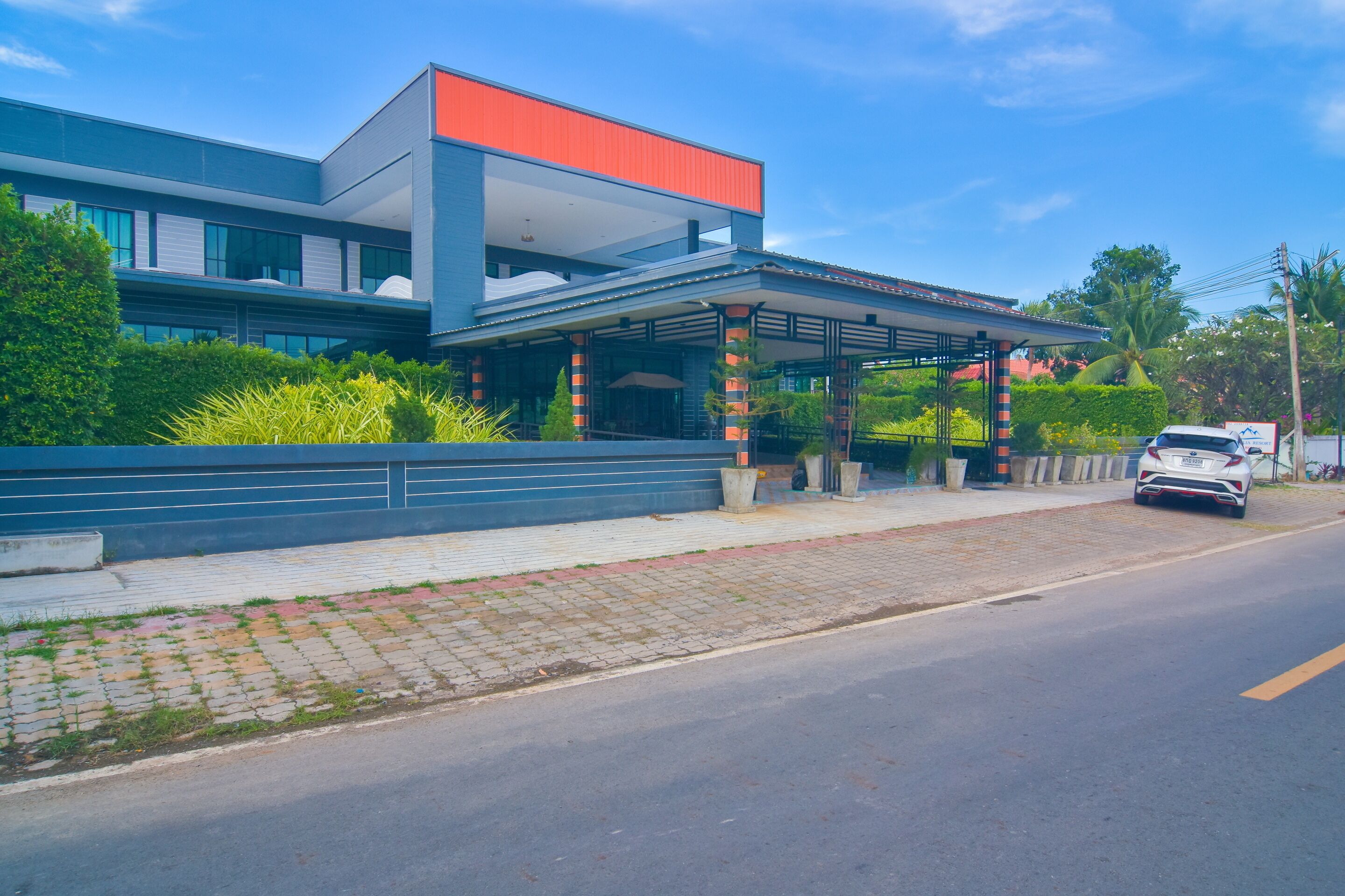 A modern building with a covered entrance, a paved sidewalk, and a road with a parked car.